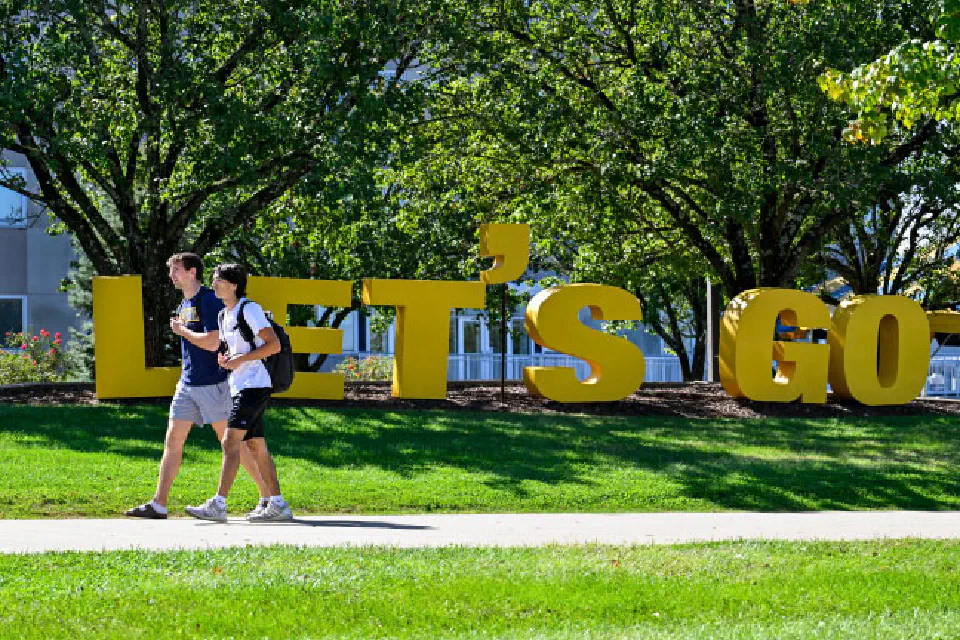 Students walking past a "Let's Go" outdoor display on campus